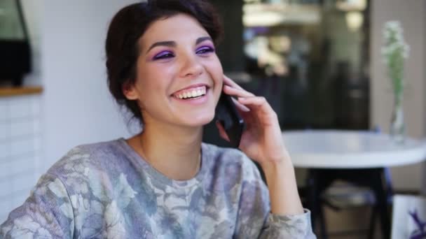 Atractiva joven mujer hablando por teléfono mientras está sentada en la cafetería. Ella sonríe. Hermosa joven mujer teniendo una conversación casual en el teléfono móvil — Vídeo de stock