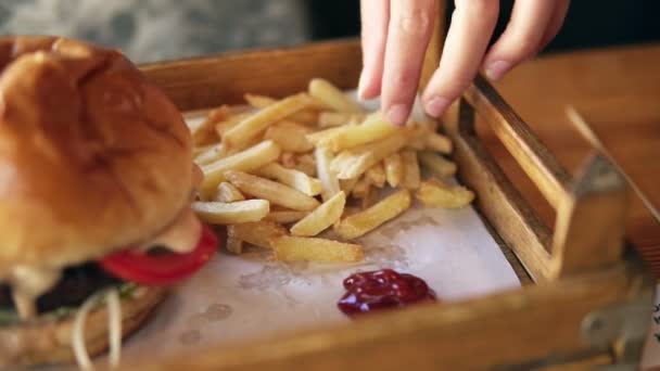 Camera moves from female hands taking french fries and showing her smiling face while eating. Slowmotion shot — Stock Video
