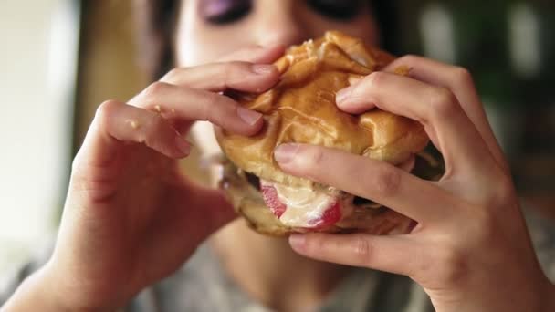特写的看法, 年轻女子咬大美味多汁的汉堡在咖啡馆。Slowmotion 射击 — 图库视频影像
