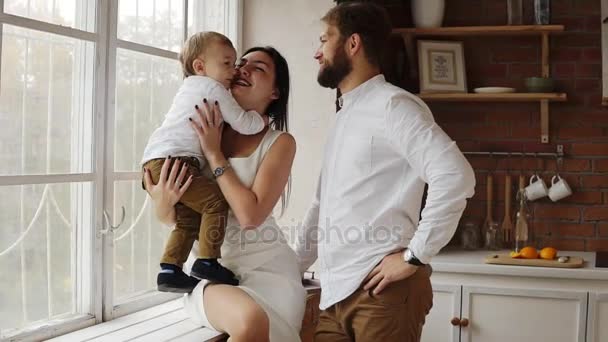 Joven madre está sosteniendo a su lindo hijo sentado en el alféizar de la ventana junto con el joven padre. La ventana está decorada con guirnalda de Navidad. Amar a la familia juntos en casa — Vídeo de stock