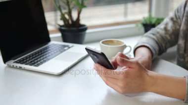 App akıllı cep telefonunda içme kahve gülümseyen ve manifatura kafede kullanan kadın. Güzel genç kadın profesyonel cep telefonu kafede. Masanın üstünde laptop