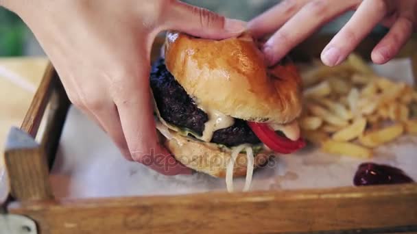 Erkek büyük lezzetli burger ahşap bir tepsiden alarak ve yemek hazırlanıyor eller. Slowmotion atış — Stok video