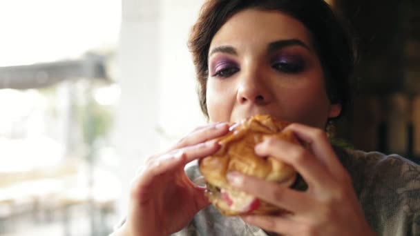 Närbild bild av ung kvinna bita stora välsmakande hamburgare i café. Slowmotion skott — Stockvideo
