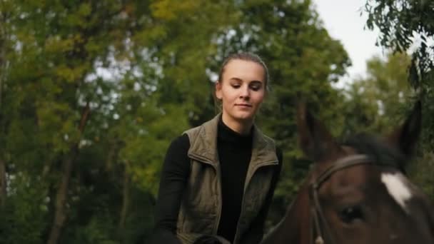 Προβολή closeup νεαρή όμορφη γυναίκα χαϊδεύοντας καφετί άλογο, ενώ κάθεται στην σέλα και βάζοντας το κεφάλι της στο το κεφάλι αλόγων — Αρχείο Βίντεο