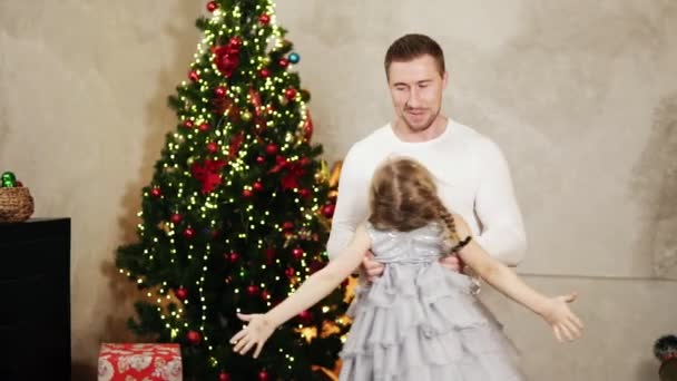 Giovane padre che si tiene per mano sua figlia e la gira intorno a casa vicino all'albero di Natale — Video Stock