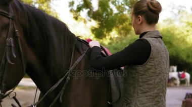 Eğitim sürmek genç çekici kadın hazırlanıyor koyu kahverengi at bir terbiye için. Bir yastık battaniye ve eyer at üzerinde hafifçe yerleştirerek kadın geri