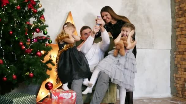 Familia de cuatro personas divirtiéndose con petardos sentados junto al árbol de Navidad decorado. Feliz padre, madre y dos hijas celebrando la Navidad juntos — Vídeos de Stock