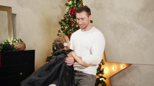 Slowmotion skott av unga far håller händerna på hans dotter och spinning henne runt hemma av julgranen. Söt familt snurrande runt hemma — Stockvideo