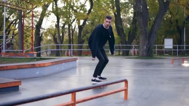 Ακραία skateboarder ακούγοντας τη μουσική στα ακουστικά λείανση κάτω ράγα στο skatepark. Slowmotion βολή — Αρχείο Βίντεο