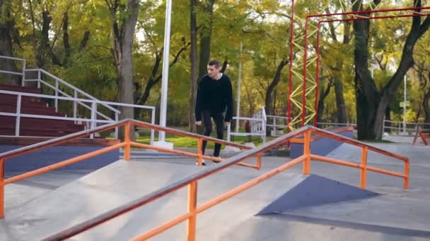 Mladí extrémní skateboardista poslechu hudby v sluchátka broušení po železnici ve skateparku. Slowmotion shot — Stock video