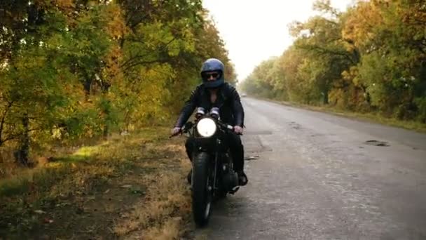 在晴朗的秋日, 黑色头盔和皮夹克的男人在路边停住了他的老式摩托车 — 图库视频影像