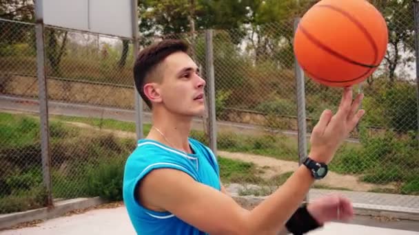 Portrait of a young serious looking basketball player spinning a basketball on the street playing field. Slowmotion shot — Stock Video