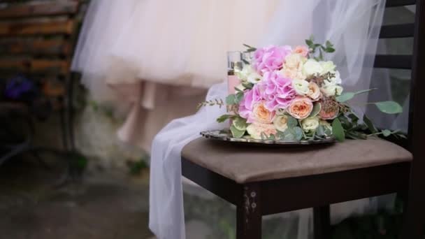 Mooie bruids boeket op de tabel met mooie trouwjurk en bruids toebehoren op de achtergrond. Trouwjurk op schouders, voor ceremonie. Mooie bruiloft boeket en jurk voor de bruid — Stockvideo