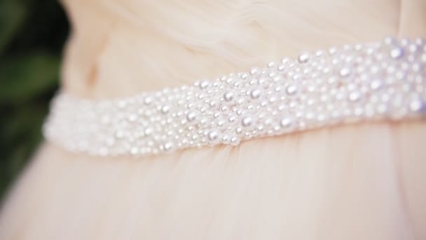 Closeup view of beautiful wedding dress with pearls hanging on the tree branch. Slowmotion shot — Stock Video