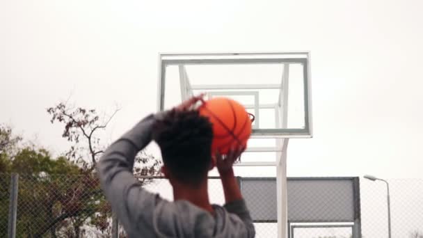 Vista posterior de un irreconocible jugador africano saltando y lanzando una pelota en un aro de baloncesto, la pelota golpea el ring y anota. Disparo en cámara lenta — Vídeos de Stock