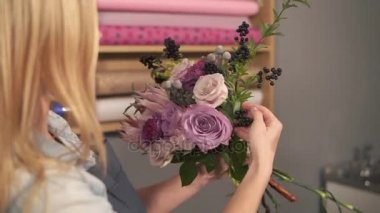 Modern buket düzenlenmesi ve çiçekler nasıl birleştirilir arayan kadın sarışın çiçekçi yan görünüm. Yakışıklı çiçek dükkanı sahibi buket yapım onun çiçek dükkanında çalışıyor. Slowmotion atış