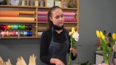 Genç kadın Çiçekçi Çiçek dükkanında modern buket düzenlenmesi Slowmotion vurdu. O krem gül ve Sarı laleler birleştirir