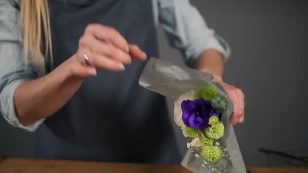 Vista de cerca de las manos de la florista femenina envolviendo un ramo de flores en papel decorativo. Disparo en cámara lenta — Vídeo de stock