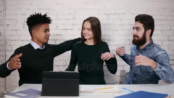 Több-etnikumú változatos üzleti csapat ölelni egymást az asztalnál, modern irodában ülve. Slowmotion lövés — Stock videók