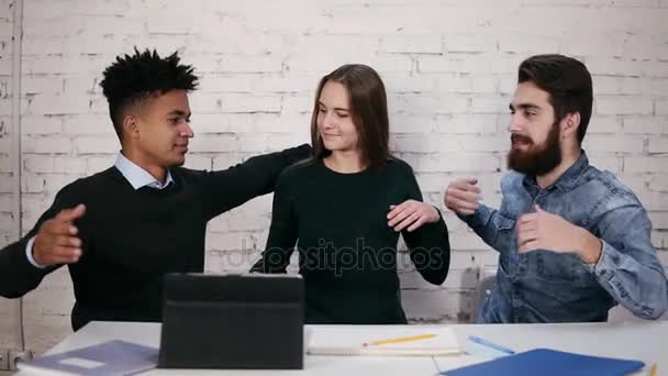 Equipo de negocios multiétnico y diverso que se abrazan mientras se sientan a la mesa en la oficina moderna. Disparo en cámara lenta — Vídeo de stock