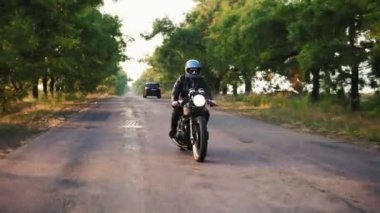 Önden Görünümü gri kask ve deri ceket ve ekose gömlek sonbahar güneşli bir günde bir asfalt yolda motosiklet sürme bir adam. Ağaçları ile kahverengi ve sarı bırakır yolun