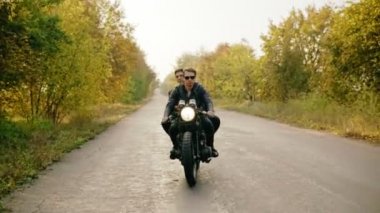 Sonbaharda orman yolu üzerinde motosiklet binme çift geniş izleme vurdu. Çekici bir genç adam onun helikopter arkasında oturan arkadaşı iken sürüş güneş gözlüğü