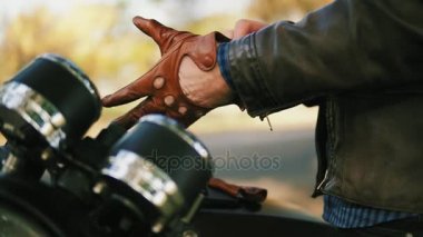 Kahverengi deri eldiven alarak ve ağır çekimde sürme için özel deri eldivenleri giyiyor tanınmayan bir motosikletçi yan görünüm