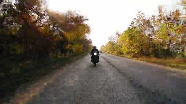 Onherkenbaar man in zwarte helm en lederen jas naderen terwijl het berijden van een motorfiets op een weg op een zonnige dag in de herfst. Toen hij de camera oogpunt outruns en gaat vooruit — Stockvideo