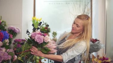 Genç kadın çiçekçi modern buket, genç yakışıklı çiçekçi iş yapma buket çiçek dükkanında düzenlenmesi. Slowmotion atış