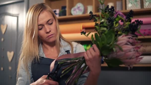 Florista loira feminina organizando buquê moderno. Bonito proprietário de loja de flores trabalhando em sua loja de flores fazendo buquê — Vídeo de Stock