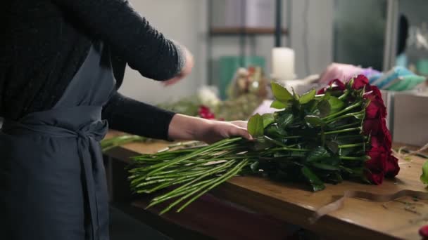 Vista de perto das mãos do florista feminino que arranja buquê moderno usando belas rosas vermelhas na loja de flores. Tiro em câmara lenta — Vídeo de Stock