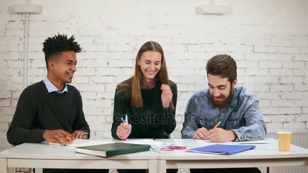 Ung afrikansk kille måleri i sin anteckningsbok och visar resultatet av hans arbete till hans kollegor. Glad mångskiftande grupp av studenter eller unga business-team arbetar med ett projekt. Slowmotion skott — Stockvideo