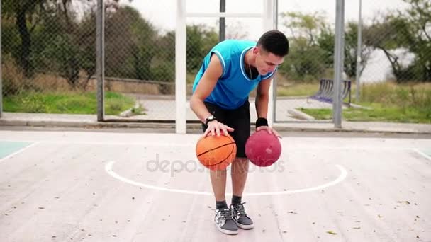 Προβολή closeup ενός νεαρού εξάσκηση μπάσκετ στο γήπεδο του δρόμου. Παίζει με δύο μπάλες ταυτόχρονα. Slowmotion βολή — Αρχείο Βίντεο