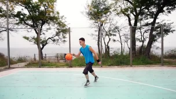 Молодой человек успешно бросает баскетбольный мяч на площадке в парке, замедленная съемка — стоковое видео