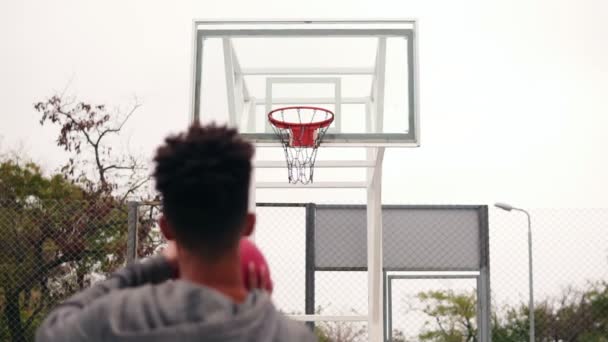 Vista posterior de un jugador africano irreconocible lanzando una pelota en un aro de baloncesto, la pelota golpea el ring y anota. Disparo en cámara lenta — Vídeos de Stock