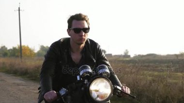 Güneş gözlüğü ve güneşli bir günde bir asfalt yolda motosiklet binme deri ceket şık havalı genç adam görünümünü portre