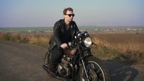 Side view of a stylish cool young man in sunglasses and leather jacket driving his chopper on a asphalt road on a sunny day. Shot in 4k — Stock Video