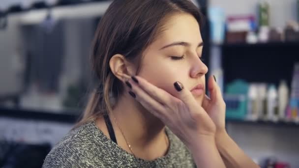 Maquiagem artista aplica creme facial no rosto de uma jovem usando as mãos. Base para maquiagem perfeita. Tiro em câmara lenta — Vídeo de Stock