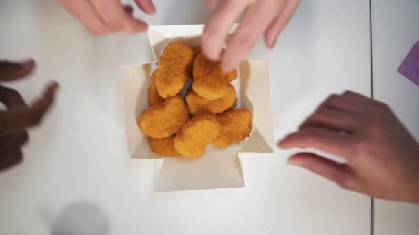 Las manos tomando pepitas de la caja de papel en la mesa. Vista superior. Gente irreconocible extendiendo armas simultáneamente para conseguir trozos de pollo. Grupo de personas hambrientas y alimentación — Vídeos de Stock