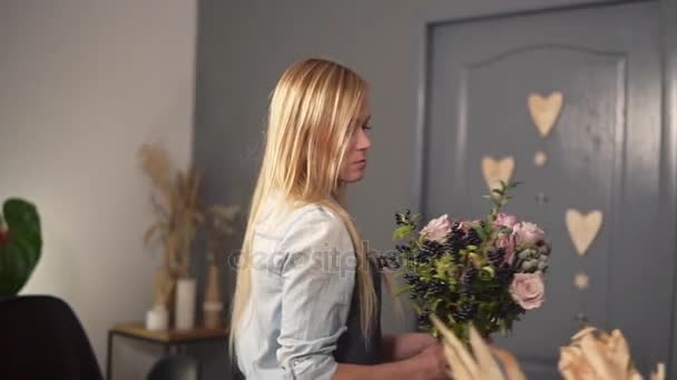 Joven florista femenina haciendo un moderno ramo de flores. Está poniendo flores en la mesa. Disparo en cámara lenta — Vídeos de Stock