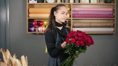 Mükemmel profesyonel çiçekçi üzerinden kırmızı gül buketi: genç çekici kadın Çiçekçi Çiçek dükkanında güzel kırmızı gül buketi düzenlenmesi. Slowmotion atış