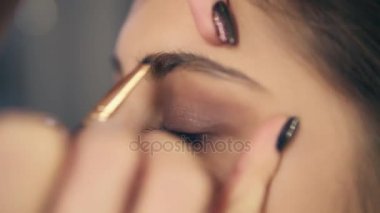 Kaşları bakım sırasında profesyonel makyaj: genç bir kadın ona kaşları almak closeup şeklinde kaş fırçası ve gölgeler. Slowmotion atış