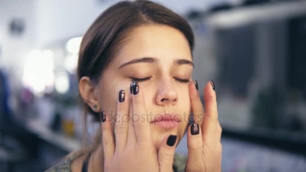Maquiagem artista aplica corretor no rosto de uma jovem usando as mãos. Ela também está fazendo massagem. Base para maquiagem perfeita. Tiro em câmara lenta — Vídeo de Stock