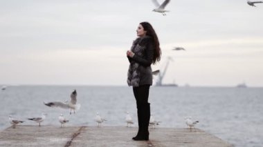 Martılar okyanus tarafından kış aylarında beslenme kürk ceket genç çekici esmer kadın. Slowmotion atış
