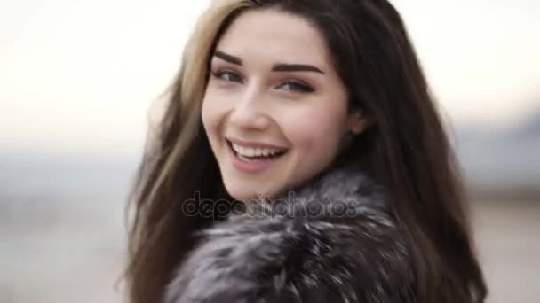 Closeup view of young attractive womans face looking in the camera and smiling. She is running forward and turning around, touching her hair. Slowmotion shot — Stock Video