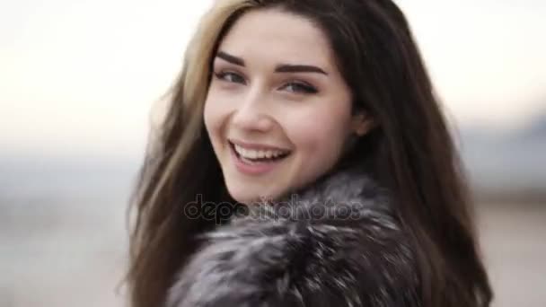 Vista de cerca de la joven atractiva cara de las mujeres mirando a la cámara y sonriendo. Ella está corriendo hacia adelante y dando la vuelta, tocándose el pelo. Disparo en cámara lenta — Vídeos de Stock