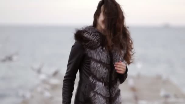 Young attractive woman looking in the camera and smiling. She is running forward and turning around, touching her hair. Sea gulls on the background. Slowmotion shot — Stock Video