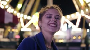 Gülümseyen ve eğlence parkı carusel arka planda ile dışarı asılı kamera bakarak at kuyruğu olan, genç güzel mutlu kız closeup görünümü. Slowmotion atış