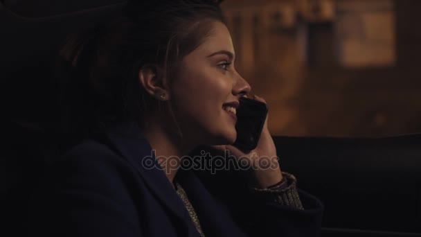 Happy smiling girl riding in a taxi at night sitting on the backseat and speaking on the smartphone. Happy woman in taxi. Night live. Slowmotion shot — Stock Video