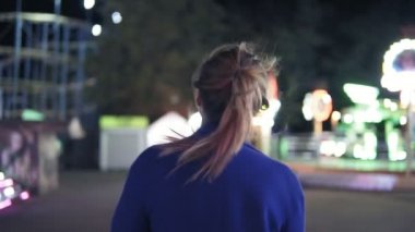 İleri sonra gülümseyerek ve eğlence parkı turistik arka plan ile dışarı asılı kamera bakarak etrafında dönerek yürüyen at kuyruğu ile genç gülümseyen kız. Slowmotion atış